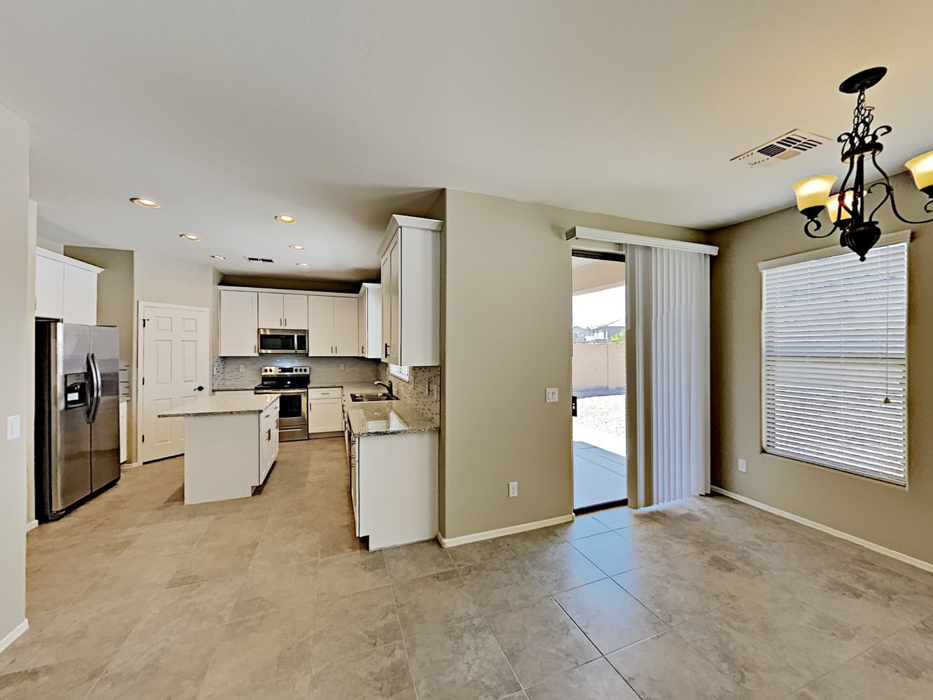 Kitchen and dining room view with beautiful tiled flooring, access to back patio, stainless-steel appliances, and island at Invitation Homes Phoenix.