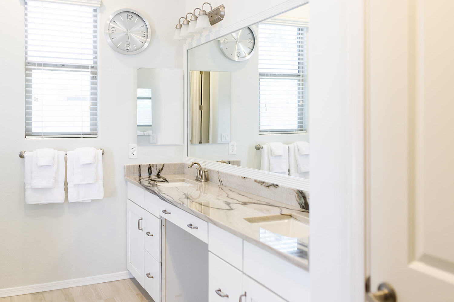 Bright remodeled bathroom with a long double vanity, white cabinetry, expansive mirror, stone counte 