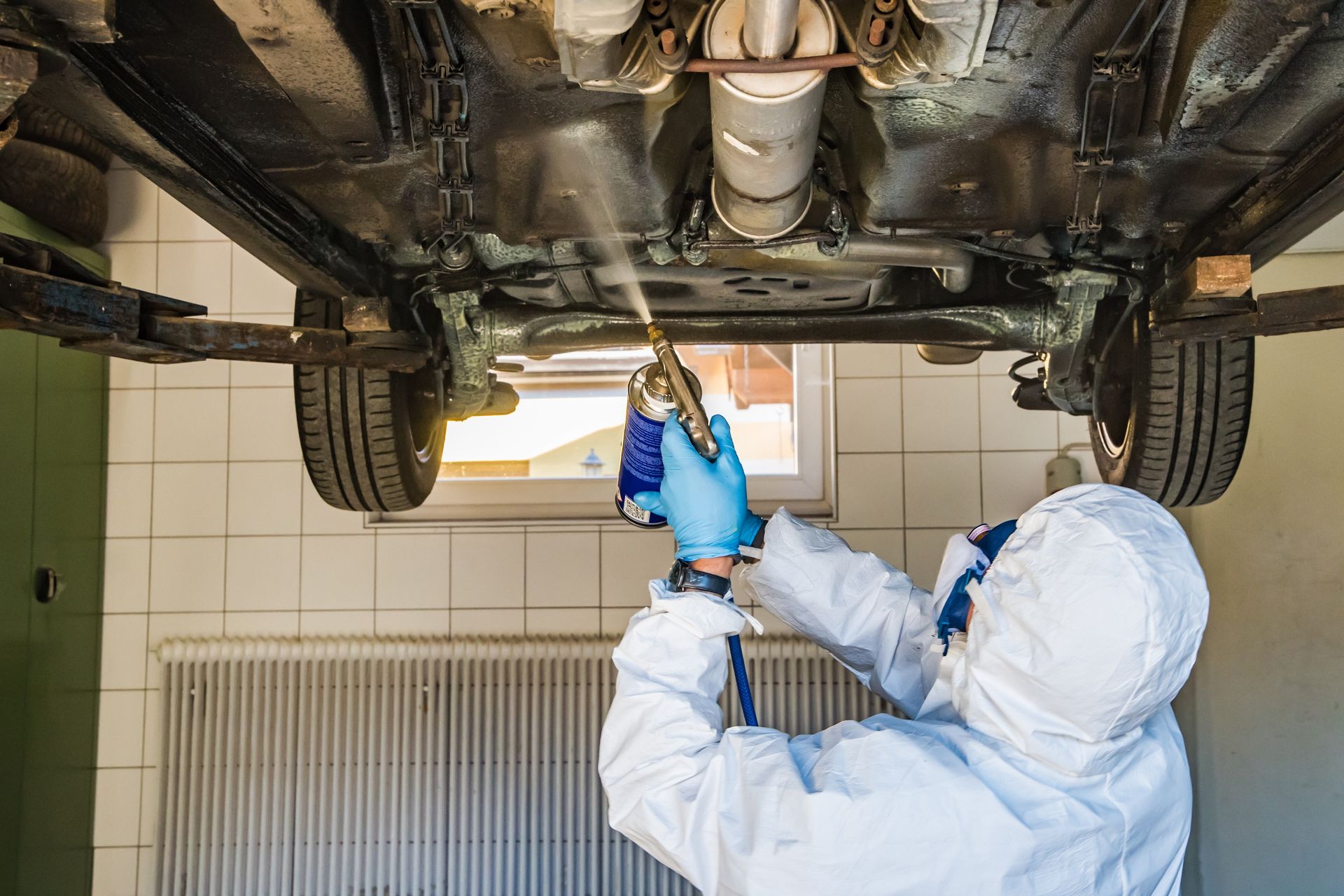 Technician applies protective coating under vehicle chassis, ensuring corrosion resistance, durability, and long-term protection using spray equipment in controlled workshop environment for automotive maintenance and preservation.