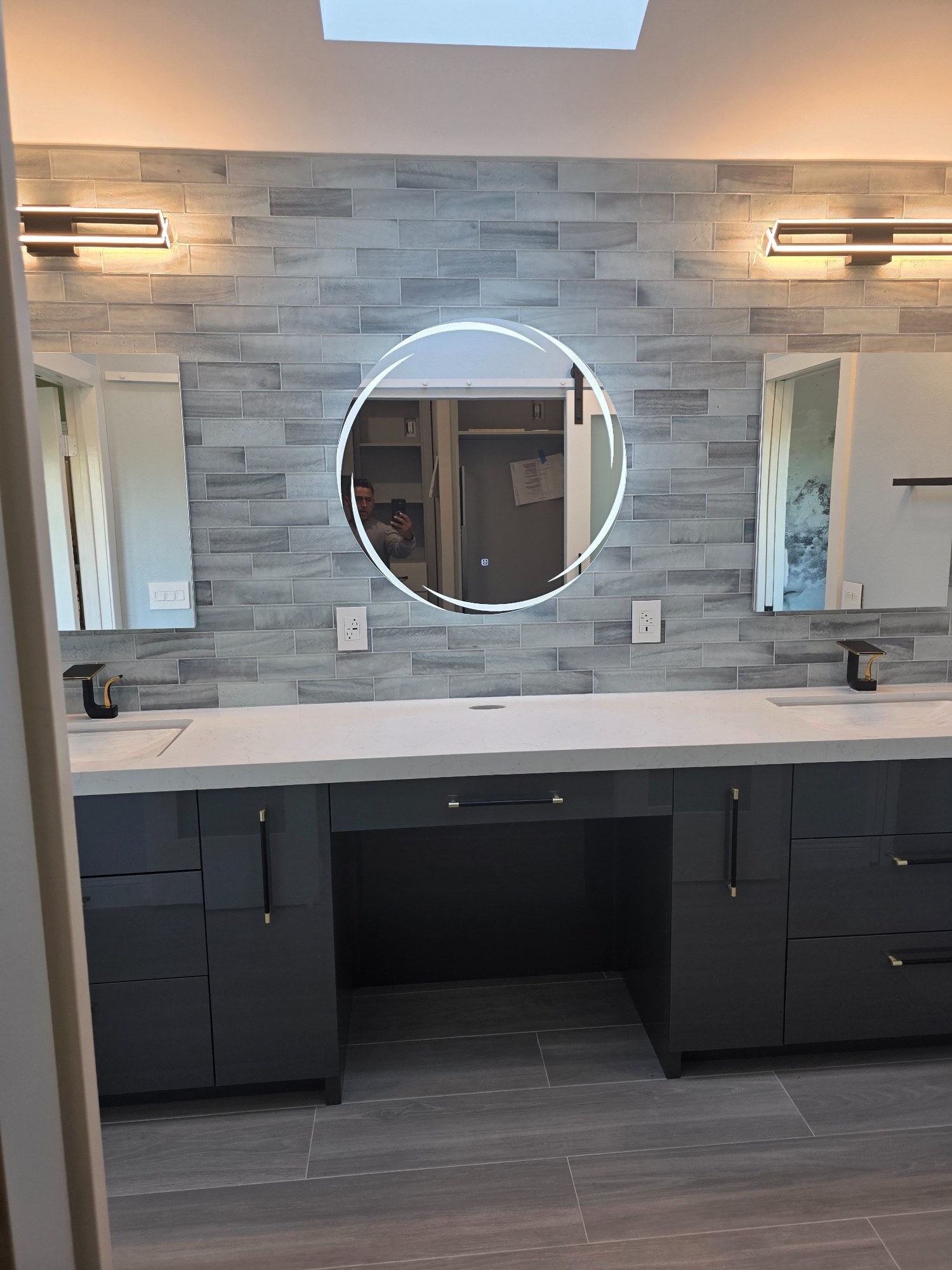 Double-vanity bathroom remodel with stone accent wall, dark cabinetry, mirrors, and modern lighting. 