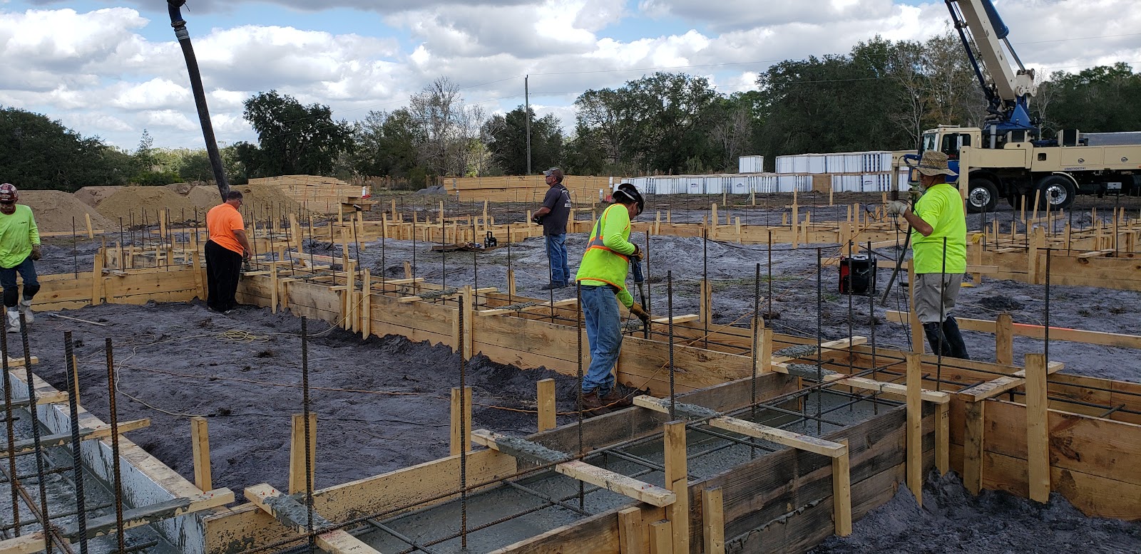 A construction crew is pouring concrete for the foundation of a building. Several workers are visibl 