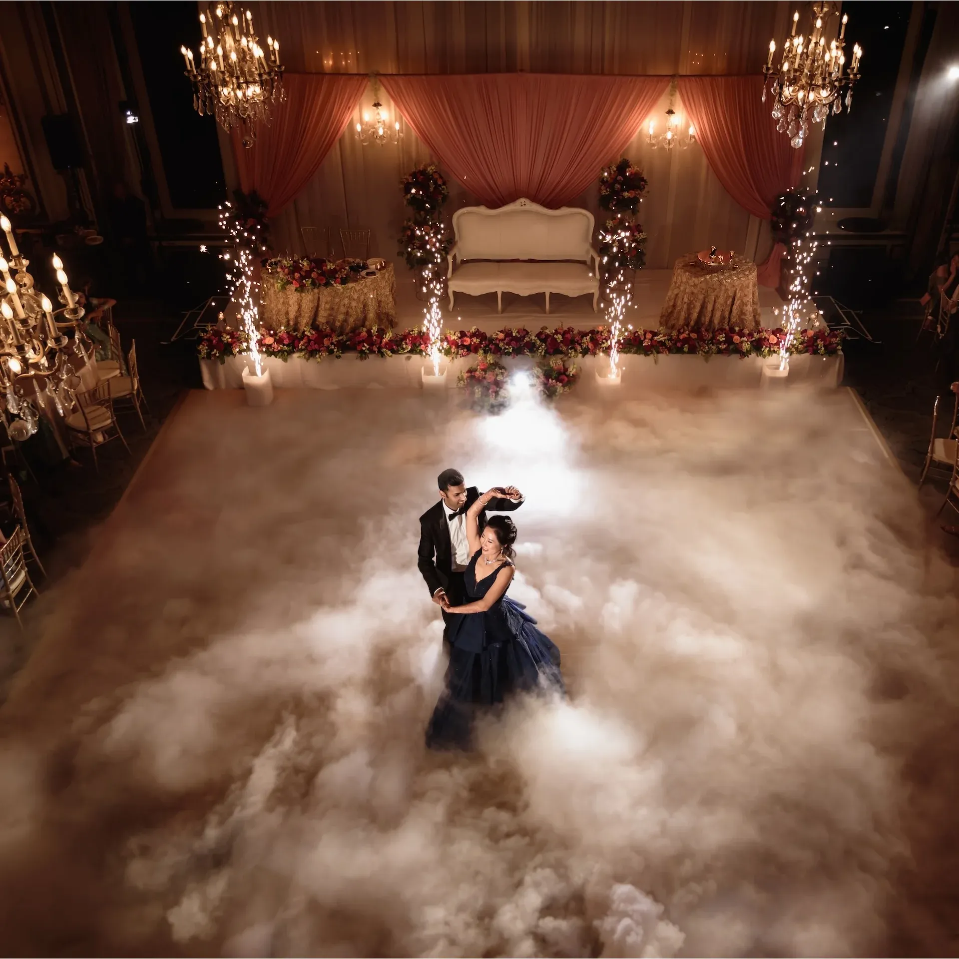 A magical first dance illuminated by the exquisite lighting design of WS Event Production Inc. Soft amber chandeliers and warm uplighting create an elegant and romantic ambiance, while dramatic cold sparklers and low-lying fog add a touch of cinematic grandeur. The carefully curated lighting complements the luxurious blush and gold theme, enhancing every detail of the floral arrangements, drapery, and décor to deliver an unforgettable experience.