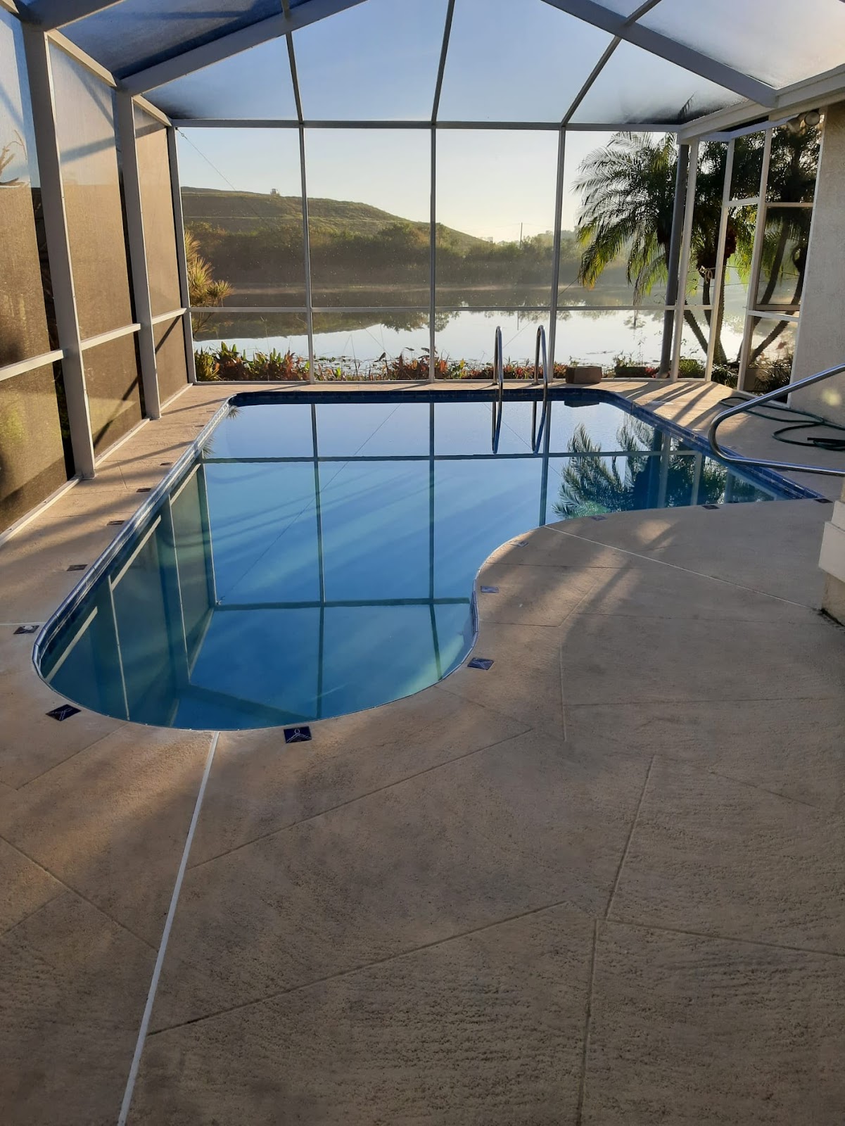 Screen-enclosed backyard swimming pool with curved edges, spacious decking, and a scenic waterfront view beyond the enclosure.