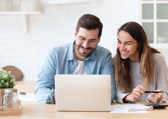 A young couple looking down at their laptop and smiling.