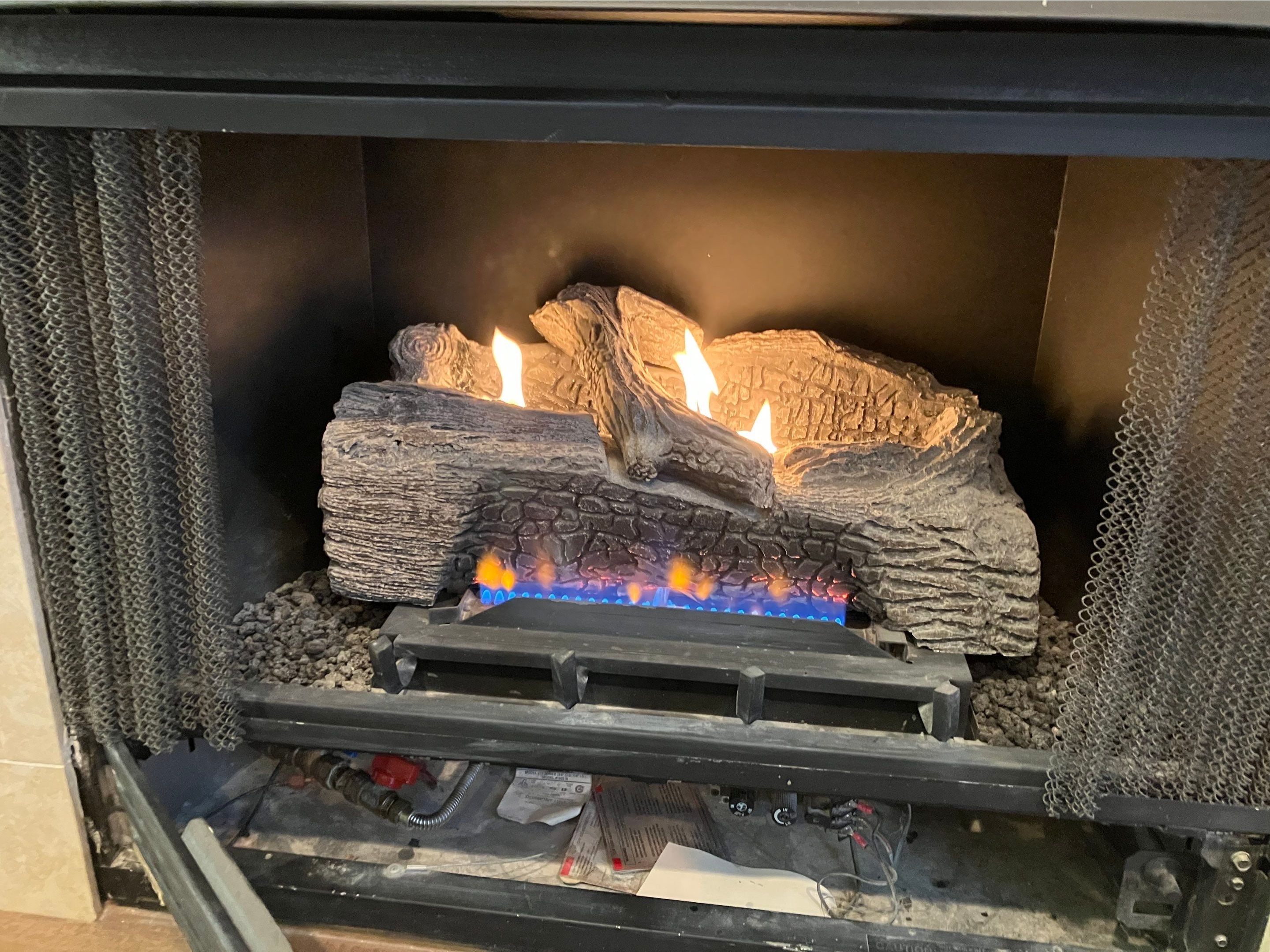 Vented gas logs burning over a blue-flame burner with a ceramic log set inside a home fireplace, ins 