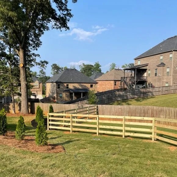 New wooden fence encloses backyard with grass, shrubs, and nearby houses.