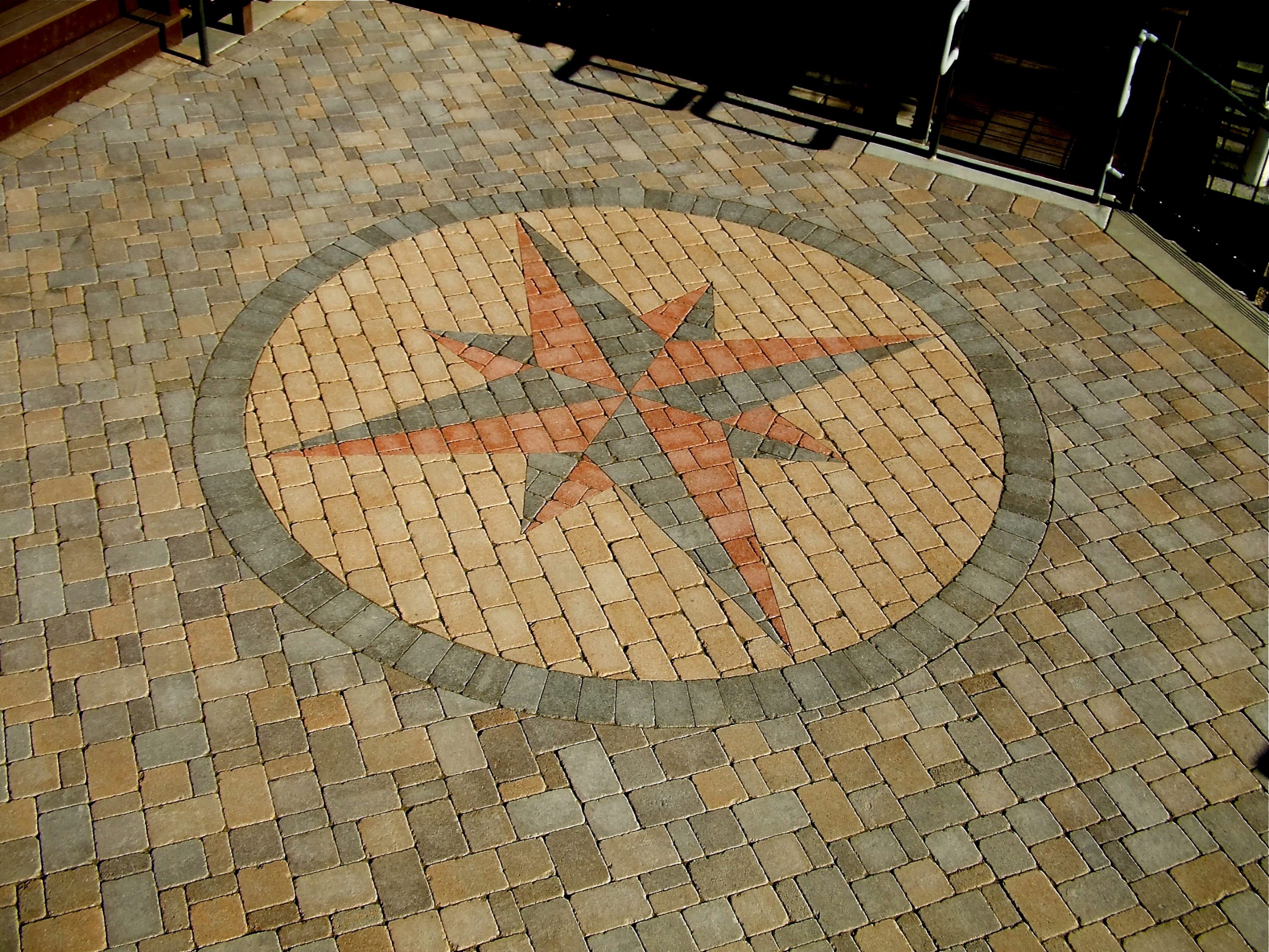 A circular compass rose mosaic in red, gray, and tan bricks decorates a sunlit paved plaza, creating a historic, ornamental atmosphere.