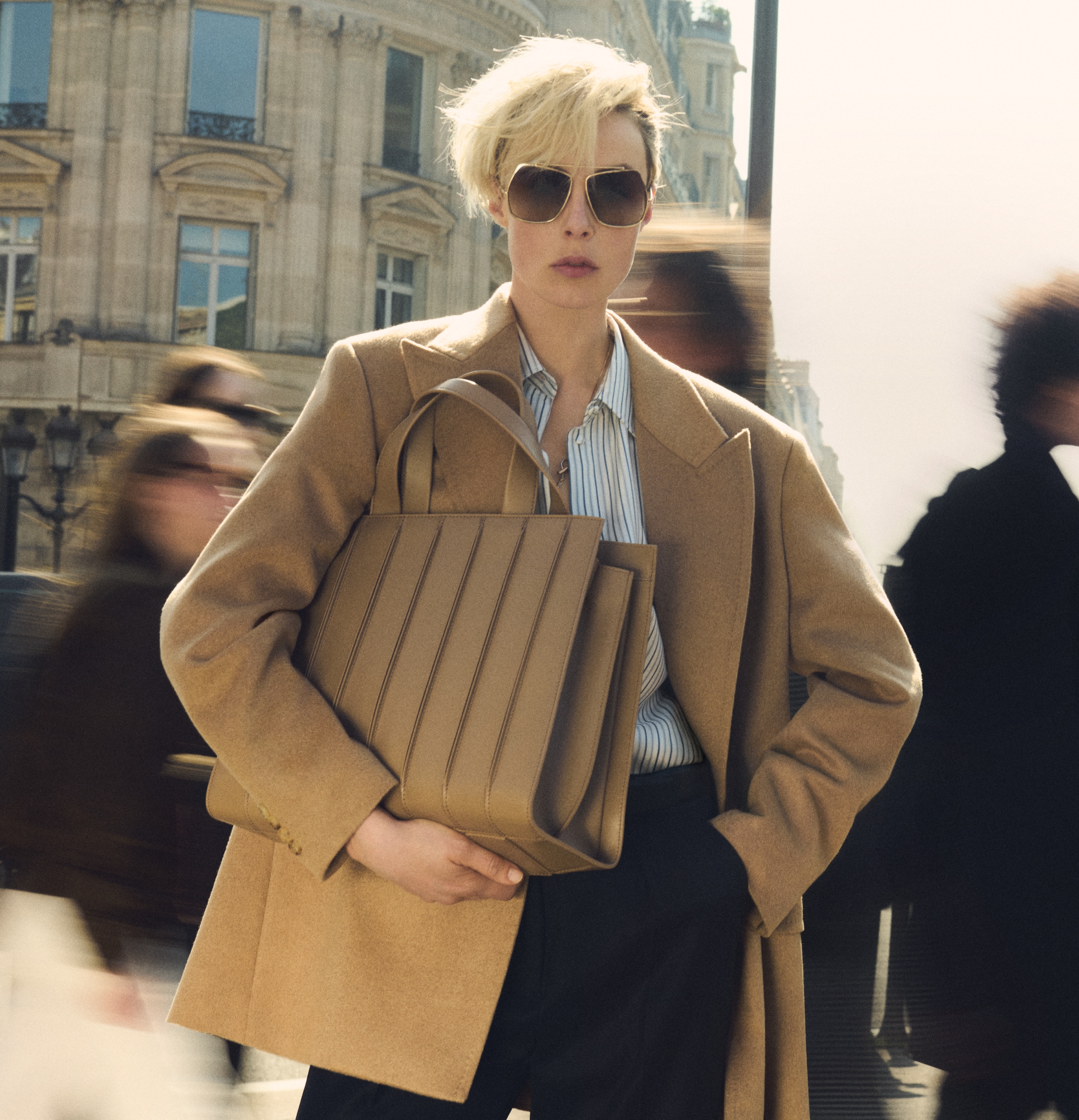 Modella in blazer doppiopetto Olimpia Jacket di Max Mara color cammello, con occhiali scuri, camicia e dettaglio borsa Whitney Bag 7 di Max Mara large, in pelle color cammello con cuciture verticali in risalto.