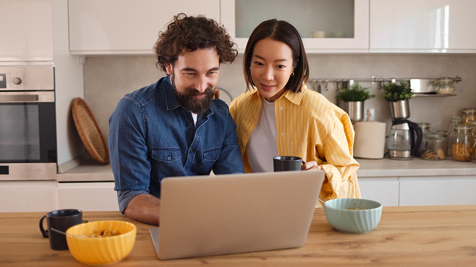 Two people looking at a laptop in a kitchen.