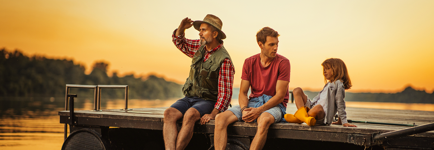 A multigenerational family sitting on the edge of a dock at sunset.