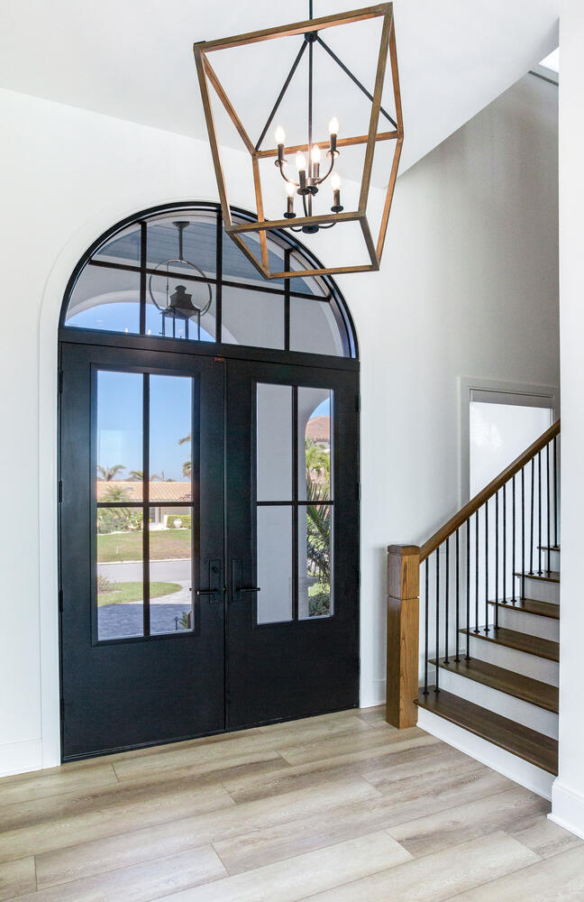 Elegant custom home entryway featuring arched glass doors, a staircase with modern railing, natural light, and a statement geometric chandelier.
