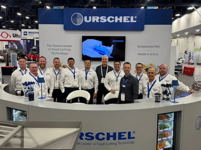 Urschel Laboratories team at a trade show booth showcasing food cutting technology, with branded displays emphasizing their leadership in food processing equipment.