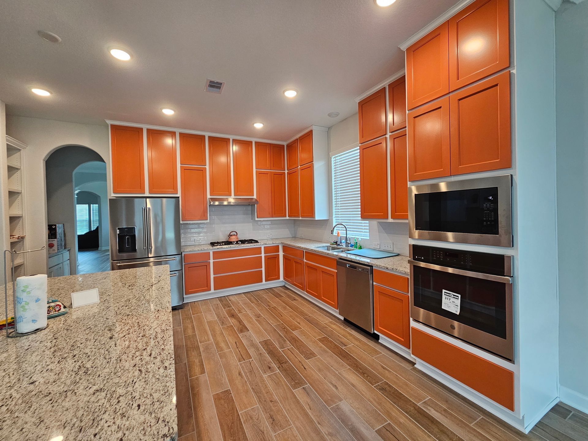 Vibrant kitchen featuring bold orange painted cabinets, granite countertops, stainless steel appliances, and warm wood-look flooring, creating a unique, energetic space with striking custom color application throughout.