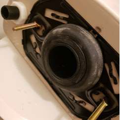 A close-up of a toilet base with the tank removed, showing the rubber gasket and mounting bolts used to secure the tank.