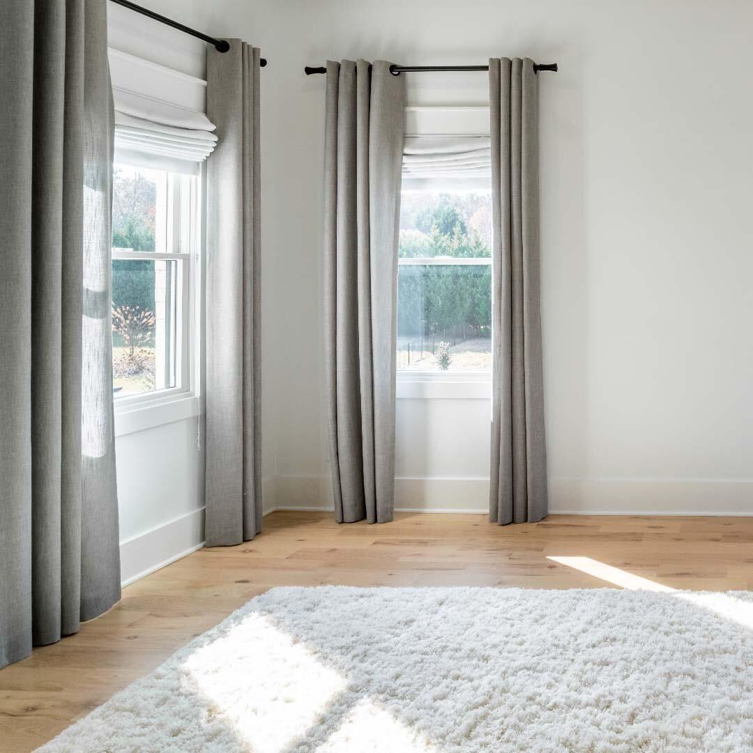 Maximize the softness of a room by mixing and matching fabric window treatments. These drapes and Roman shades are pulling double duty, perfectly accentuating the pillowy texture of this white shag rug.