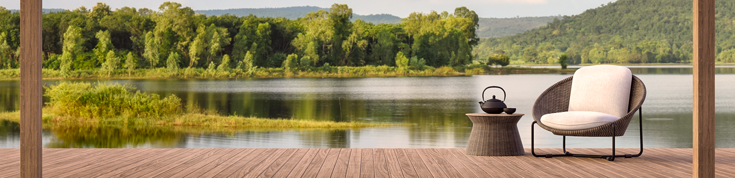A wicker armchair on a dock by a gorgeous lake surrounded by trees.