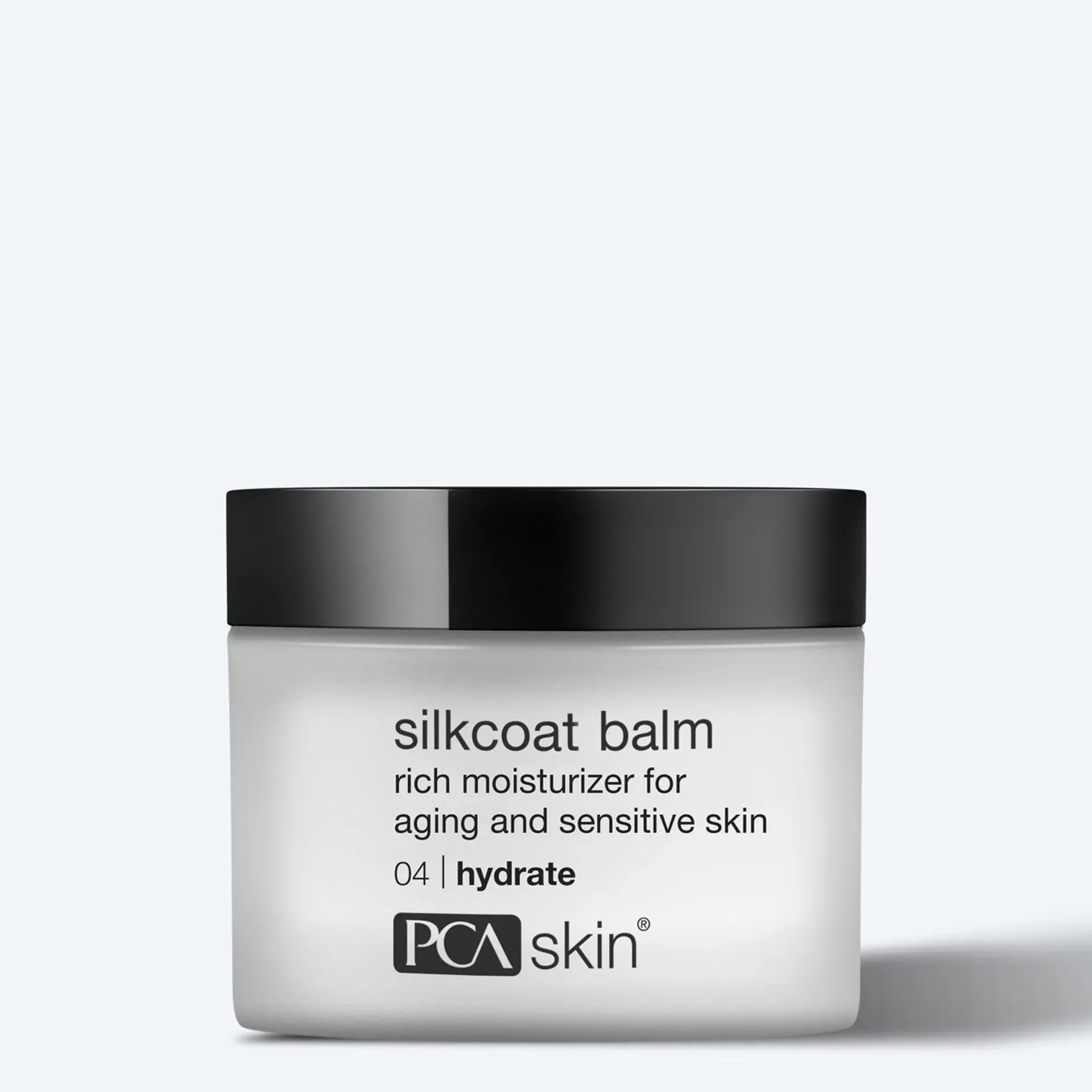 A clear product shot of a frosted glass jar of PCA Skin Silkcoat Balm, a rich moisturizer designed for aging and sensitive skin. The jar has a black cap and features the product name, description, and brand logo in black text.