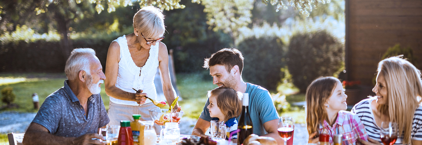A multigenerational family gathering for a meal outside on a beautiful, sunny, summer's day.
