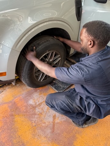 Walker Tire Point S automotive technician inspecting a vehicle's wheel and brake assembly during service.