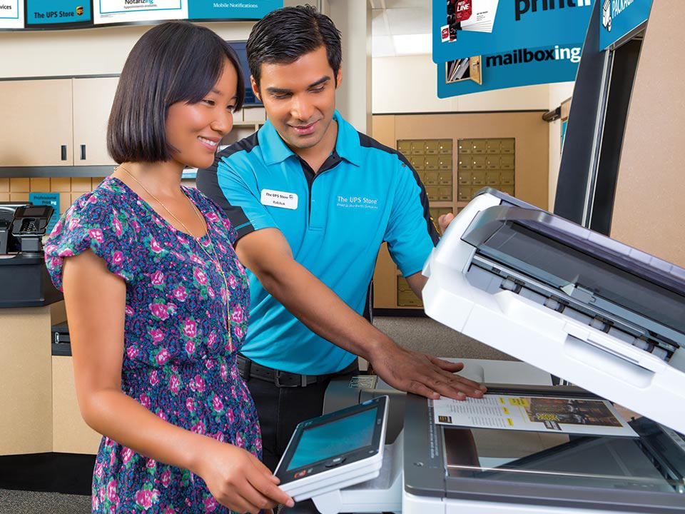 Una mujer sonriente utiliza la fotocopiadora con la ayuda de un amable asociado de The UPS Store