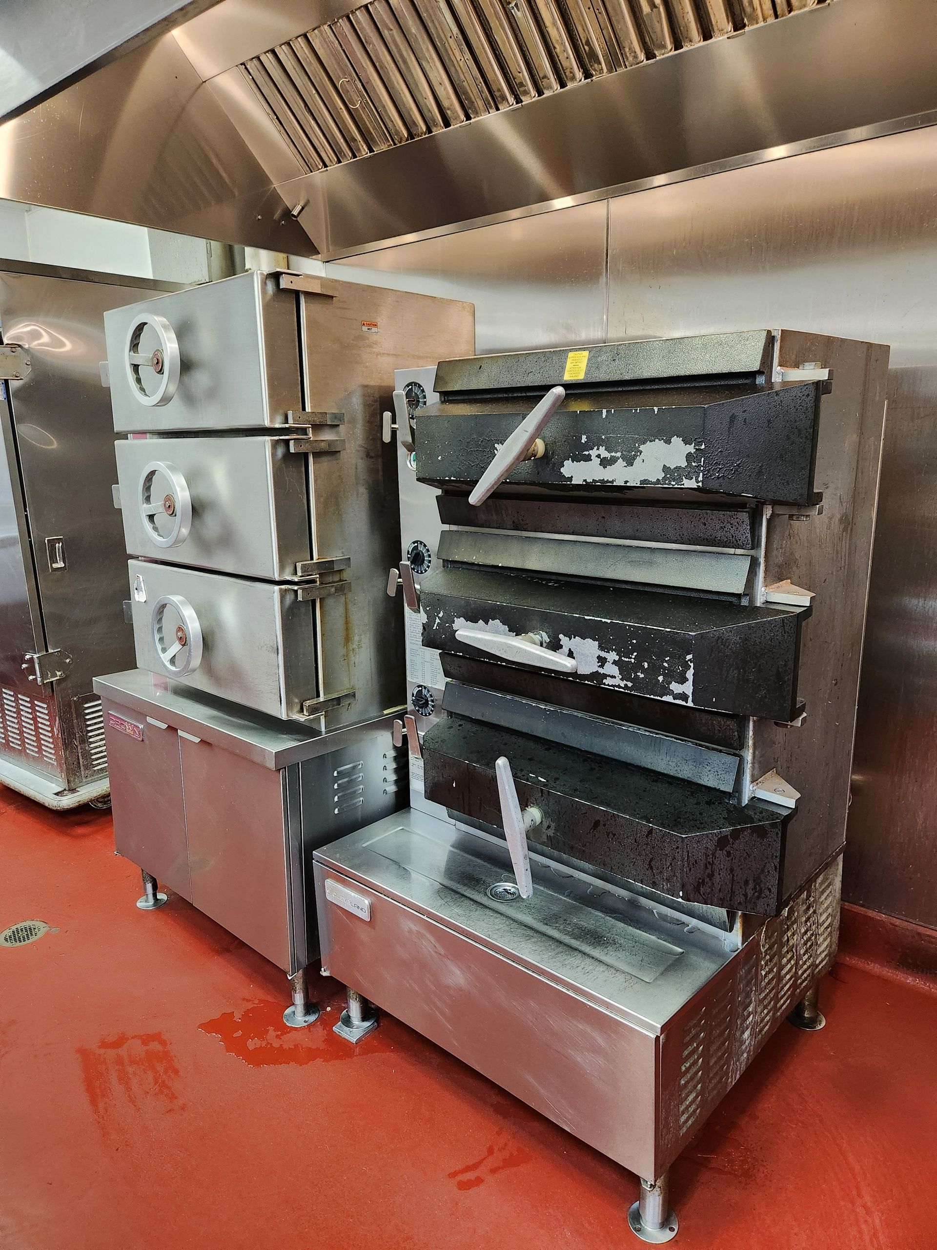 Commercial kitchen showing stacked stainless steel ovens and multiple heavy-duty cooking units, incl 