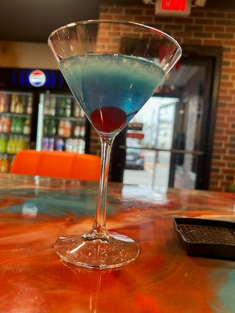 A vibrant blue martini-style cocktail served chilled and garnished with a cherry at Catramex Restaurant.