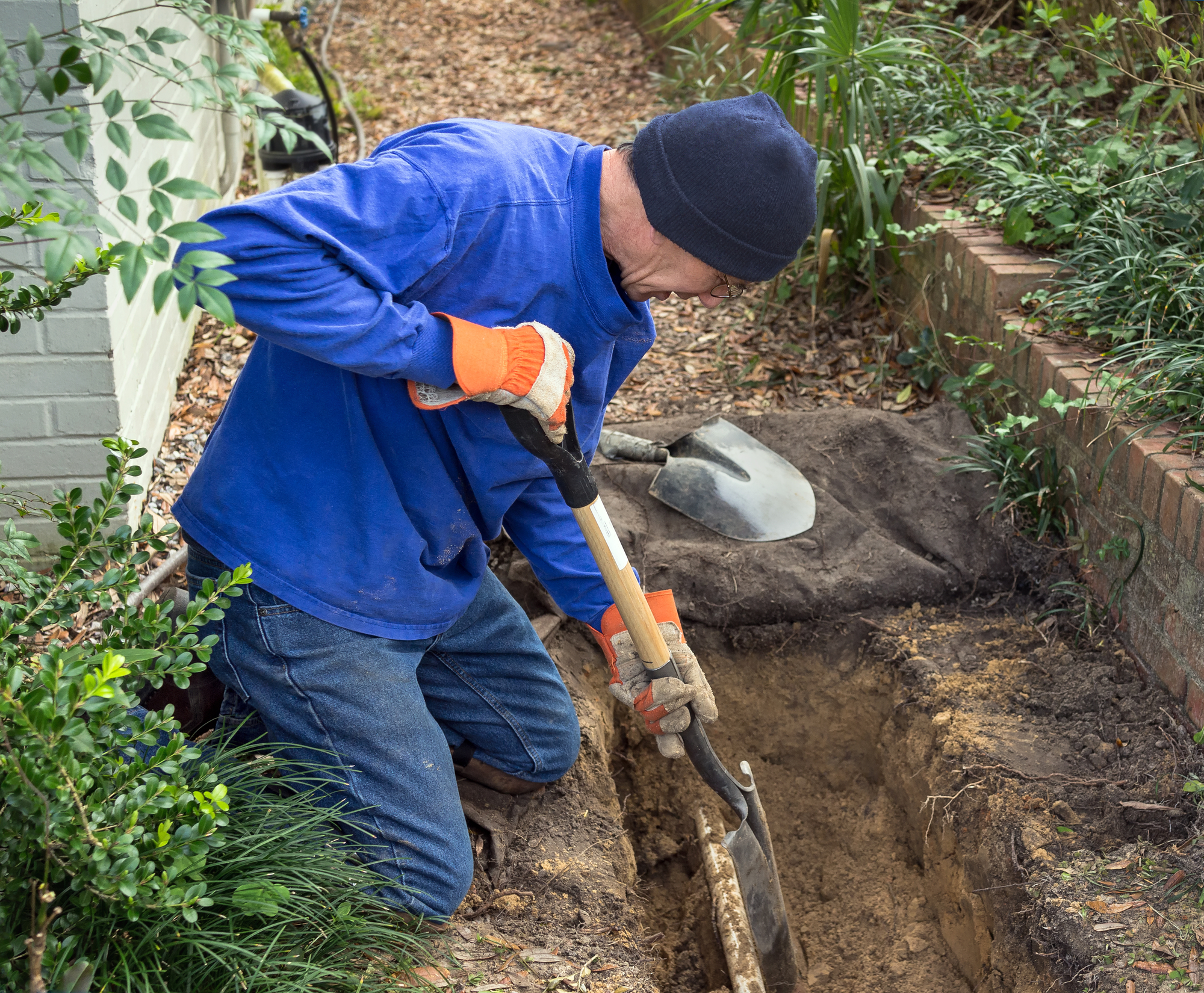 An irrigation installer digging a trench in a garden landscape to lay down underground sprinkler system lines.