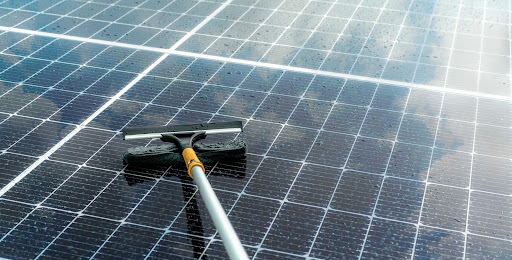 Close-up of a solar panel surface being cleaned with a dedicated brush, highlighting the removal of water and surface residue from photovoltaic glass.