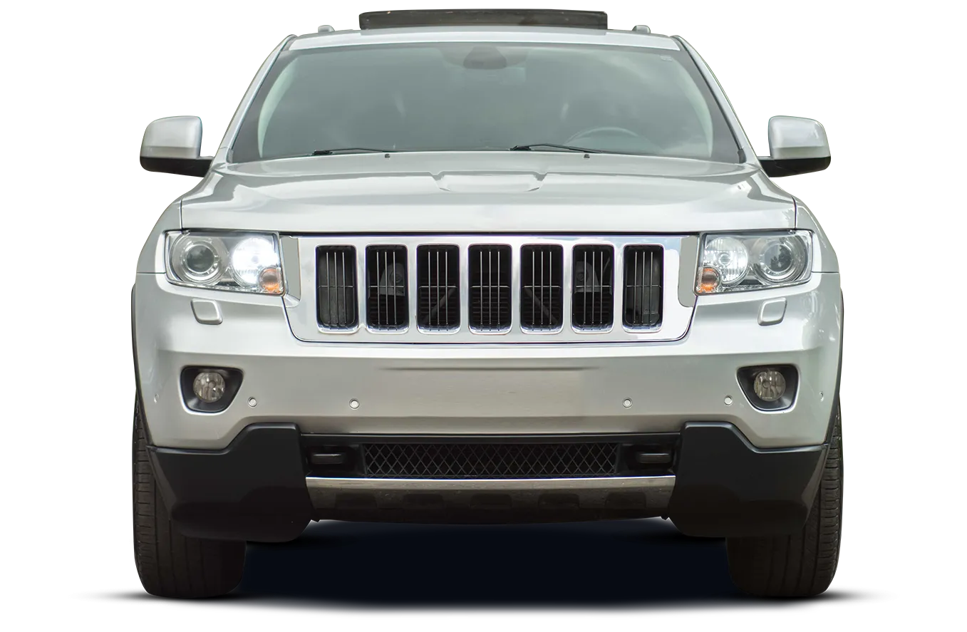 Front view of a silver Jeep Grand Cherokee with its headlights on, showcasing its iconic seven-slot grille and black bumper accents. The vehicle is isolated on a white background with subtle green and white horizontal lines suggesting a natural or outdoor environment in the upper right corner.