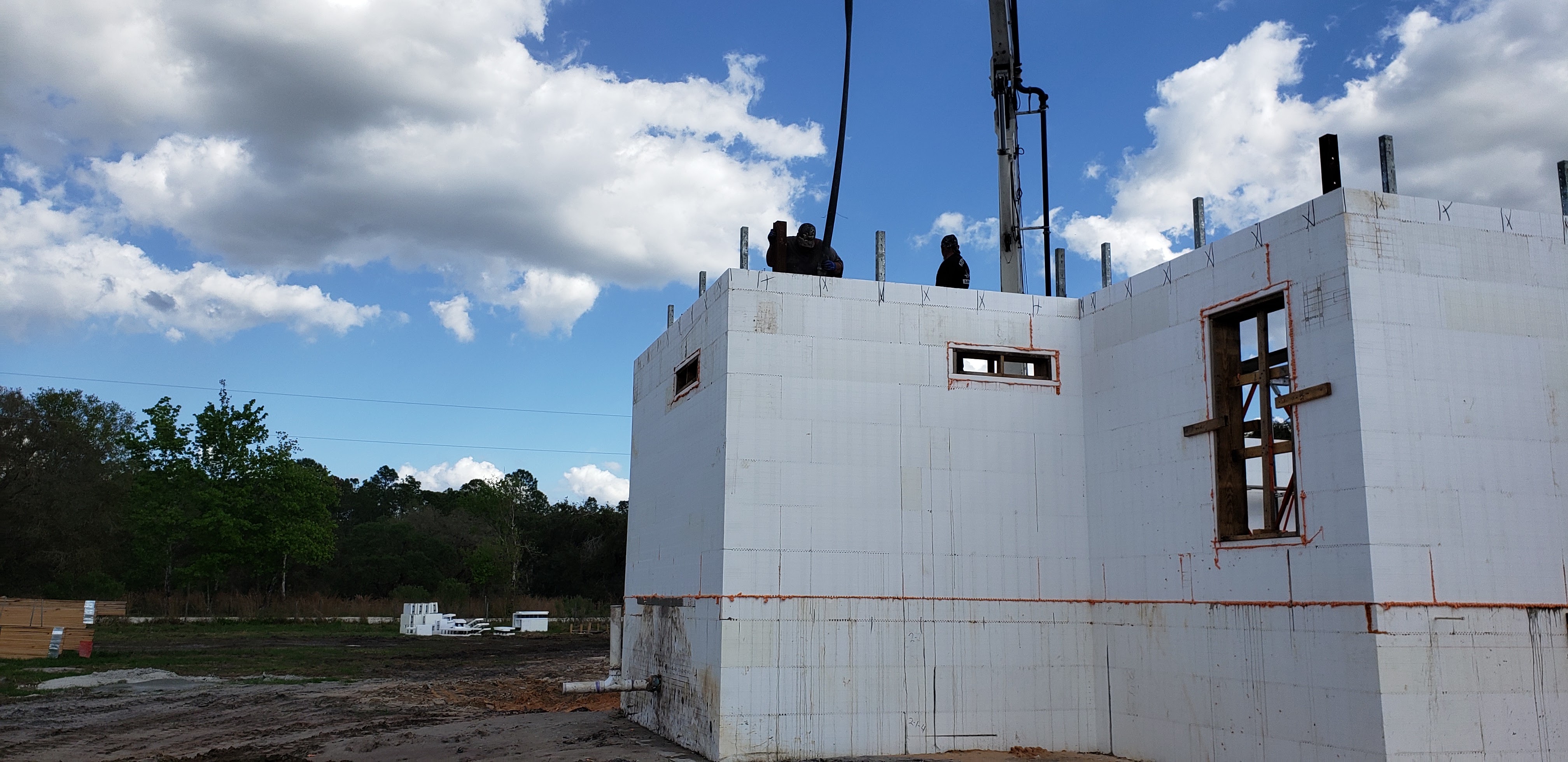A construction scene with a partially built house made of white insulated concrete forms under a blu 