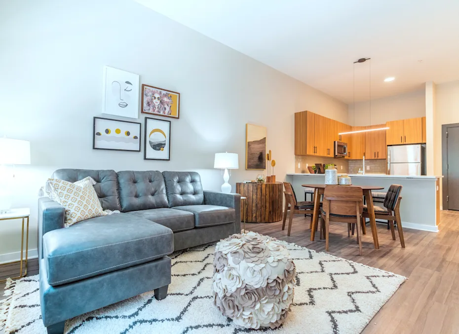 A grey sofa with a white pillow is in the middle of a room with a wooden table and chairs 