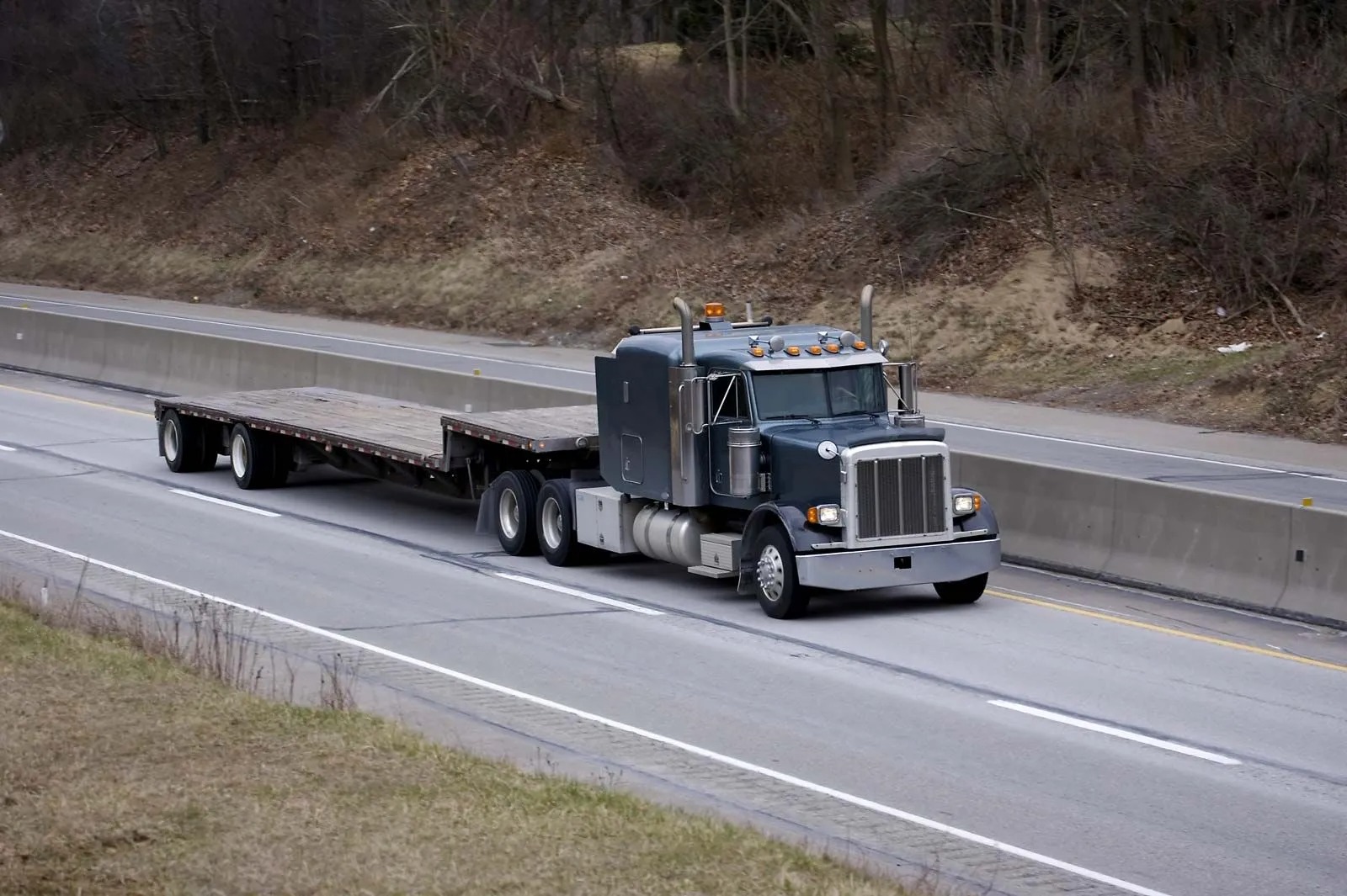 Flatbed semi truck traveling on a highway with an empty trailer. Commercial transportation vehicle available for freight pickup, equipment hauling, and specialized logistics assignments nationwide.
