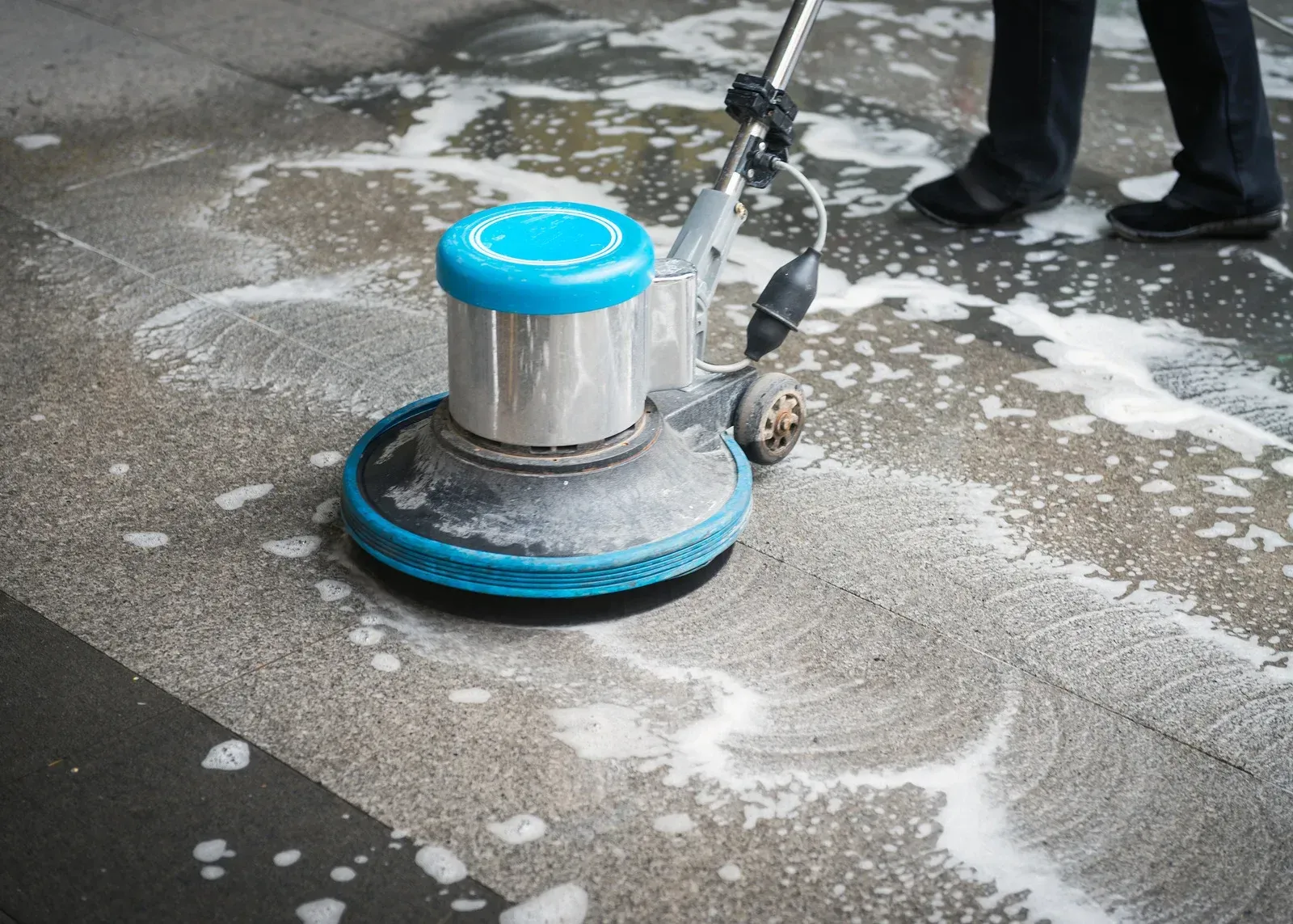 Commercial rotary surface cleaner scrubbing a concrete floor with water and cleaning solution, remov 