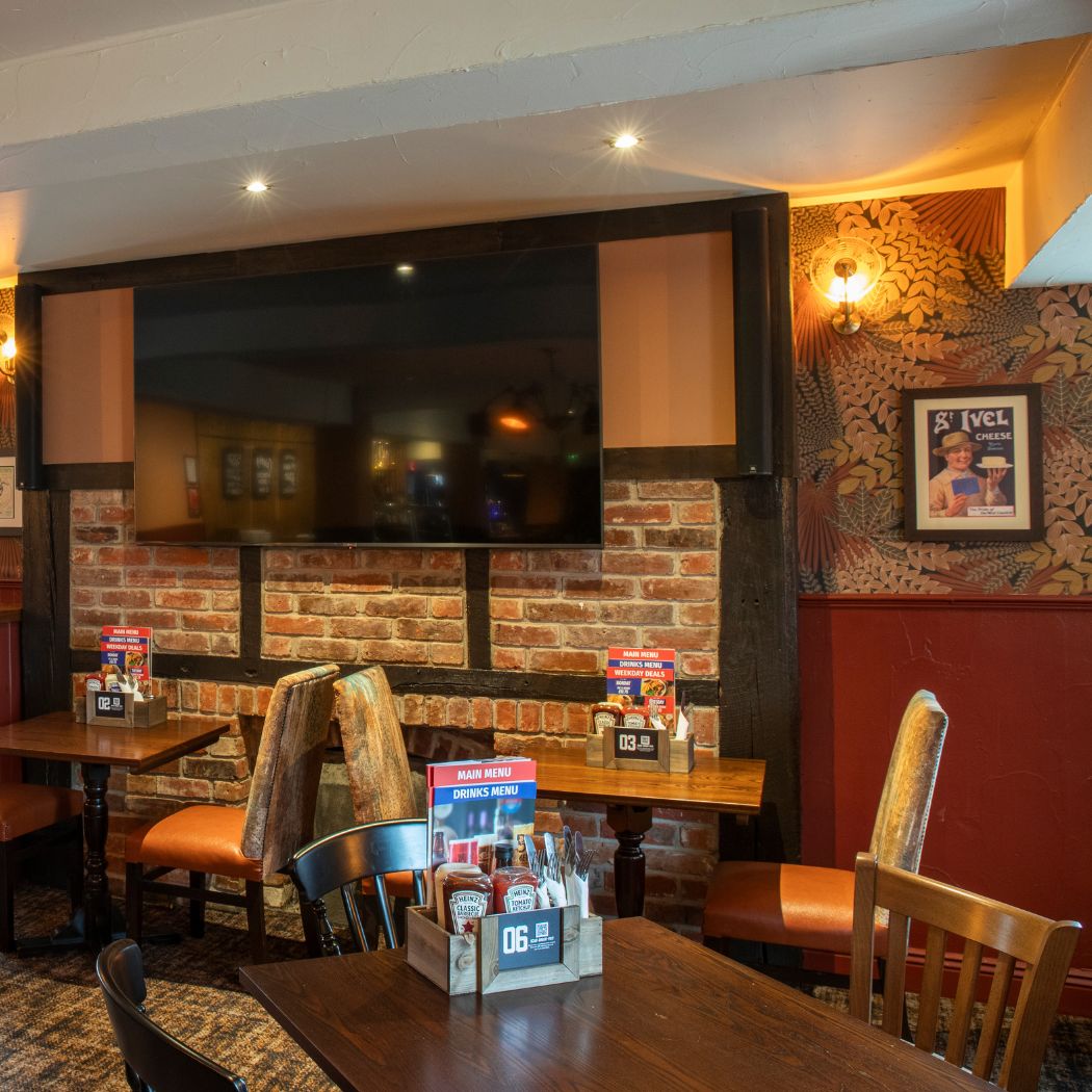 Seating area at The Arrow featuring tables, chairs and a large TV screen, offering a comfortable space for watching live sport and spending time with friends.