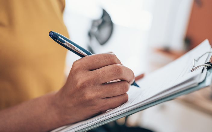 Close up of a person writing on a clipboard.