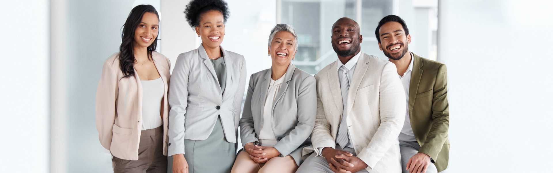 A diverse group of five professionals, three women and two men, are smiling and looking at the camer 