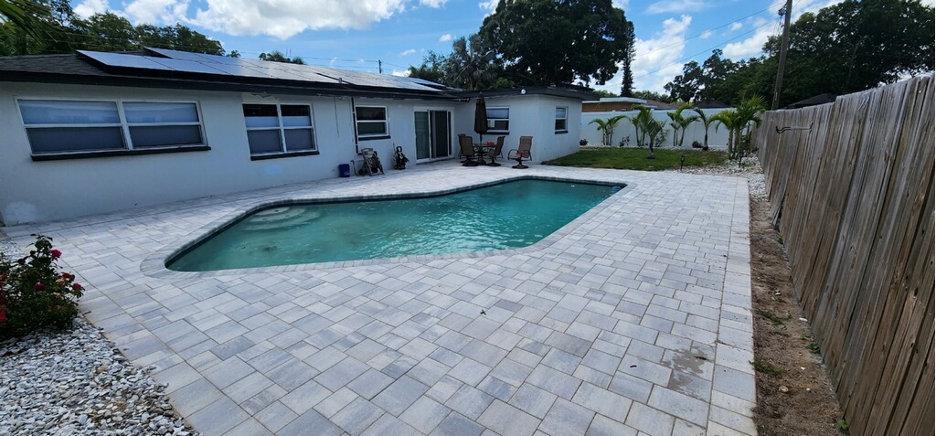 Residential swimming pool with a screened enclosure, paver deck, and private backyard setting.
