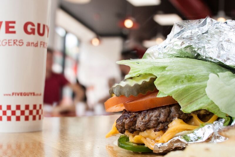 A close-up photograph of a Five Guys cheeseburger with pickles, tomatoes and jalapenos in a lettuce  Five Guys Ottawa (613)562-8119