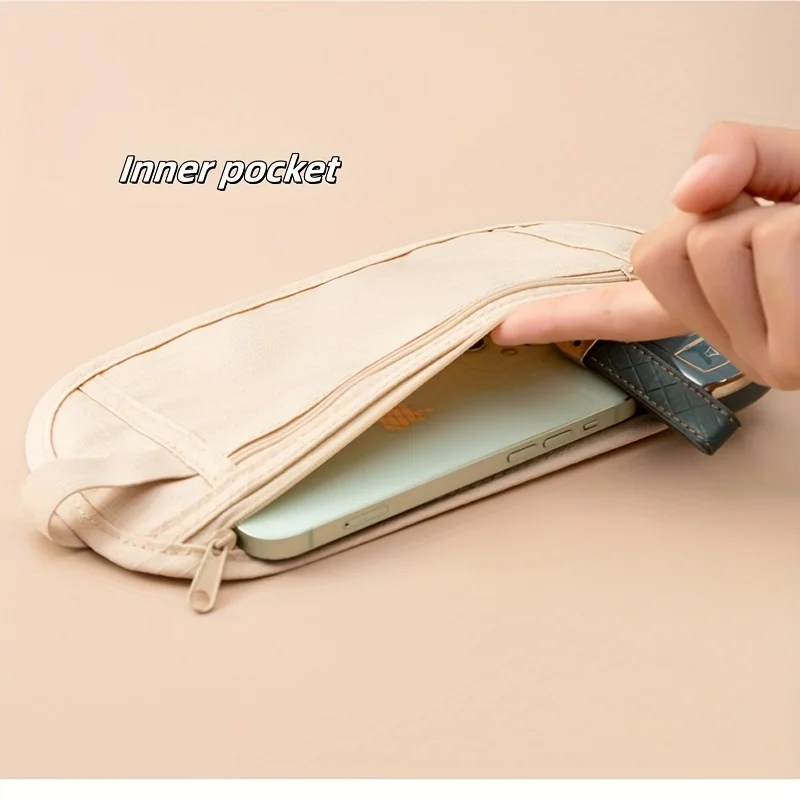 A hand is placing a smartphone and a set of keys into an inner pocket of a beige travel pouch. The pouch appears to be a sleep mask with a hidden compartment.