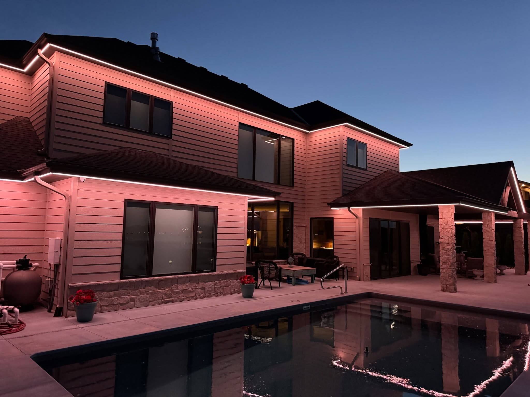 Warm architectural lighting illuminating a modern home and pool area, highlighting the exterior walls and roofline at night.