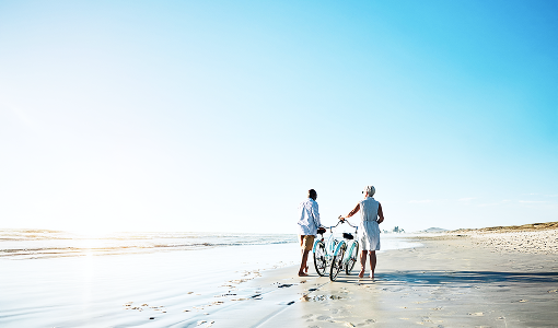 People walking with bikes on a beach.