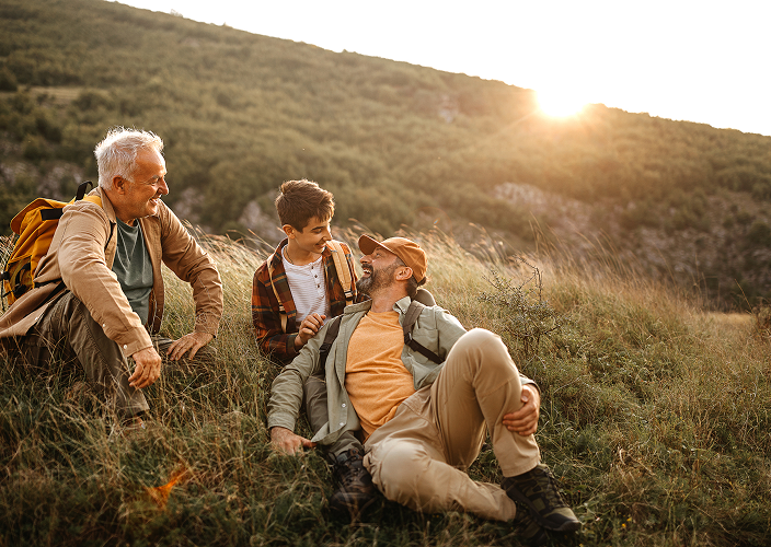 A grandfather with his son and grandson resting during a hike at golden hour.
