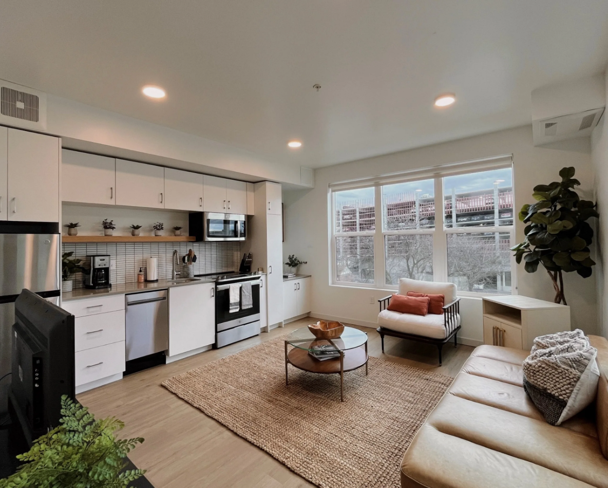 An open-style living room with view into the  kitchen, cozy seating area with a coffee table, and large windows