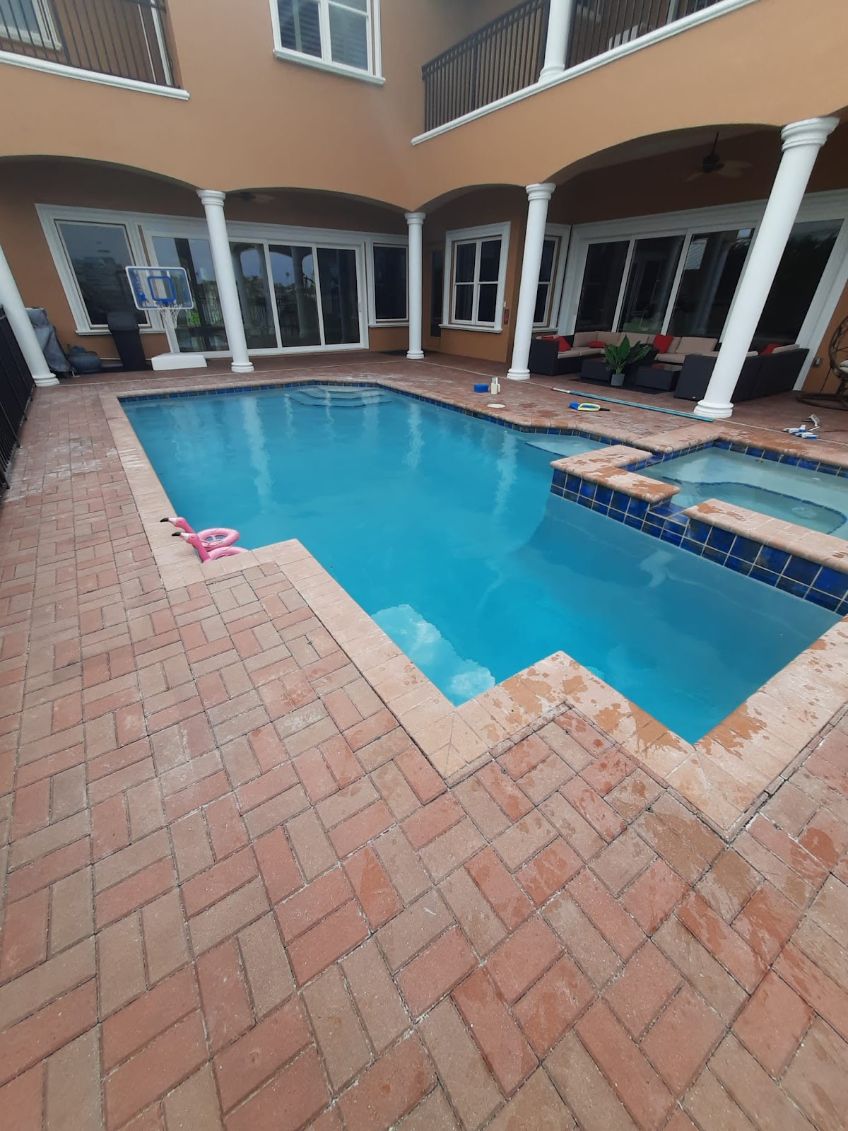 Courtyard swimming pool with clear blue water, brick paver decking, and a multi-story home surrounding the patio.