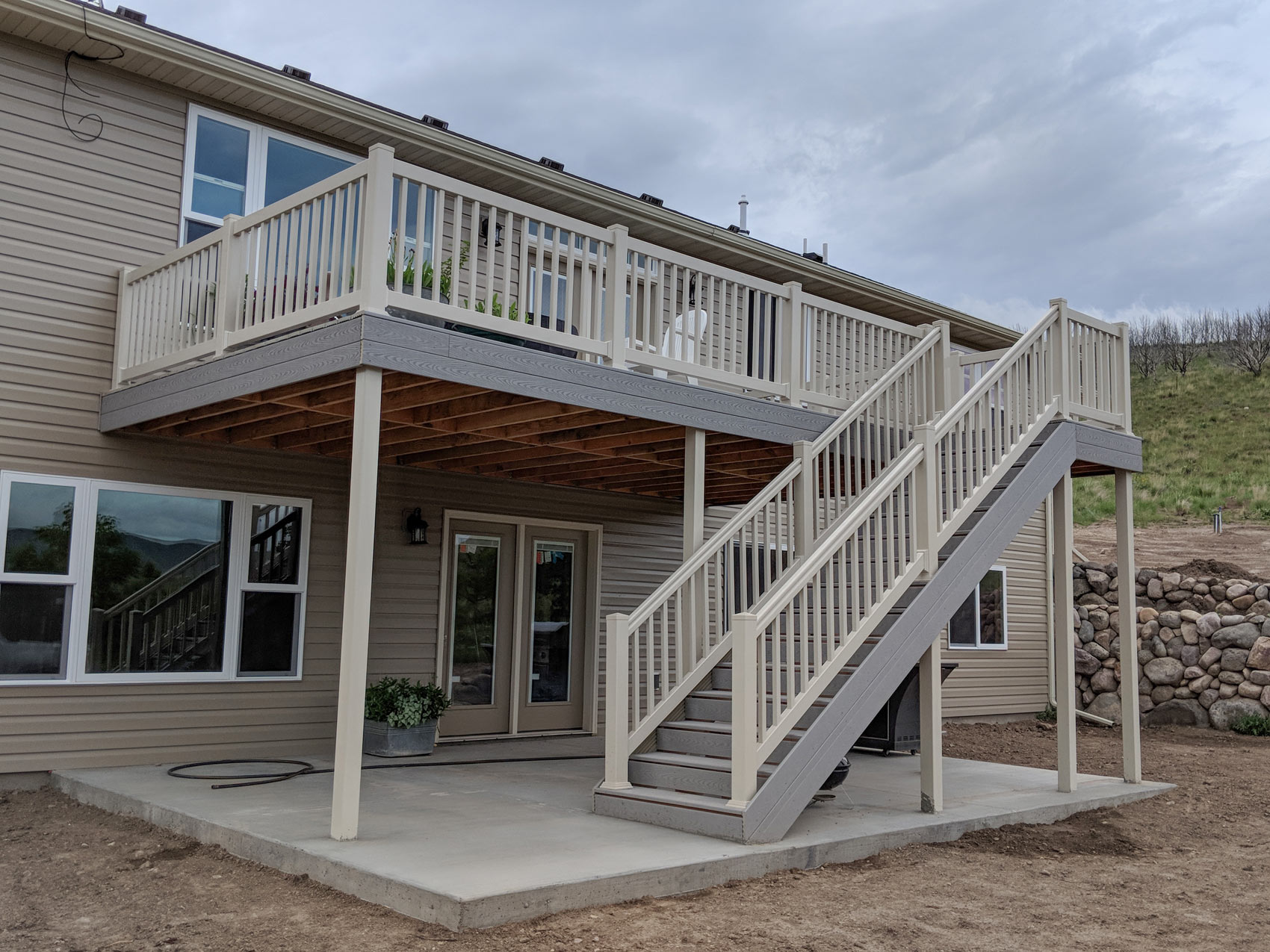 Expand your outdoor living space with this multi-level composite deck and patio combination by DeckPro LLC. This design provides a clean upper-level platform for dining and entertaining, connected by a wide, durable staircase to a lower-level concrete patio. Perfect for homes with walk-out basements, this project maximizes functionality while maintaining stunning, open views.