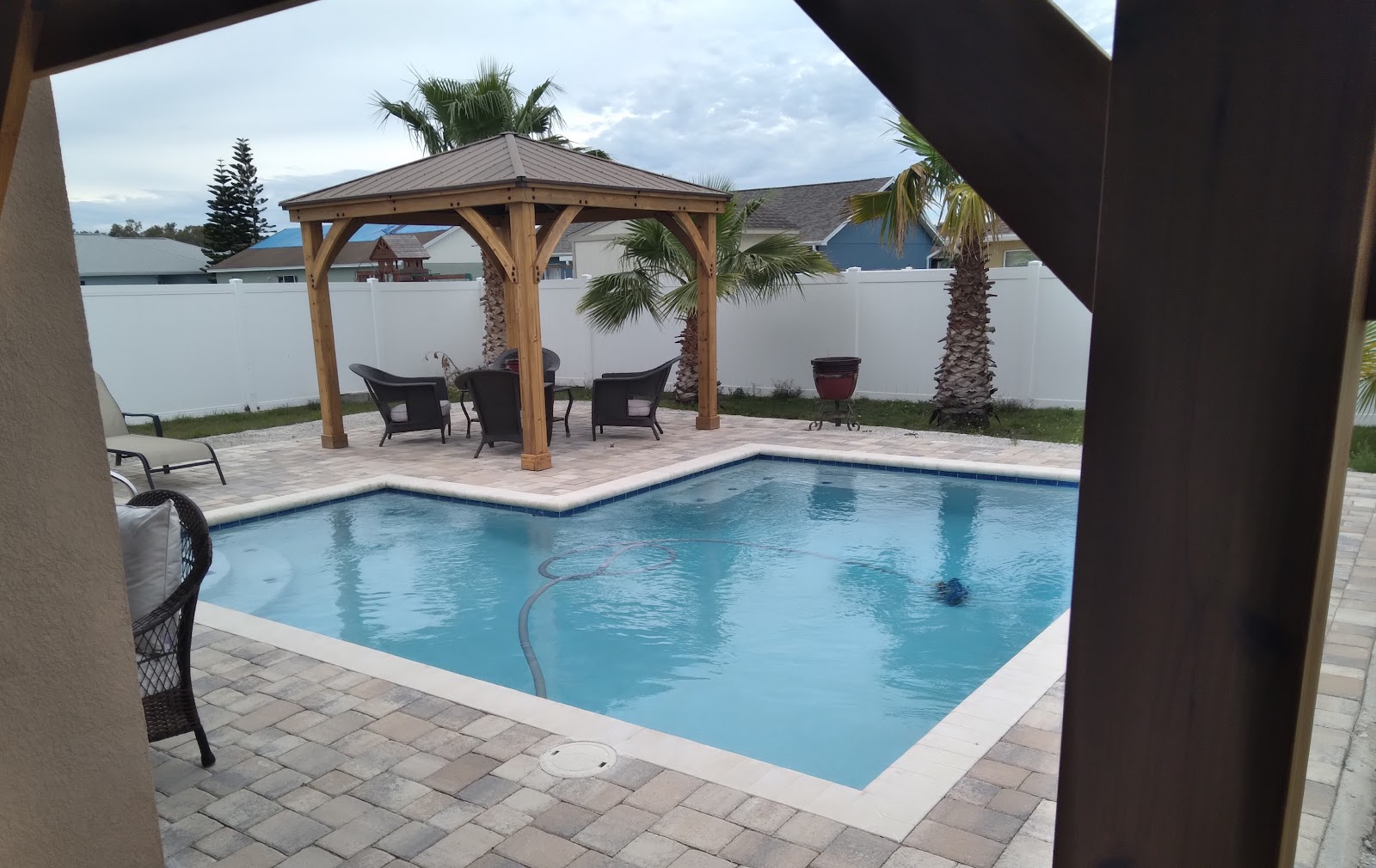Waterfront backyard swimming pool with light paver decking, a covered gazebo, and peaceful views of the water.