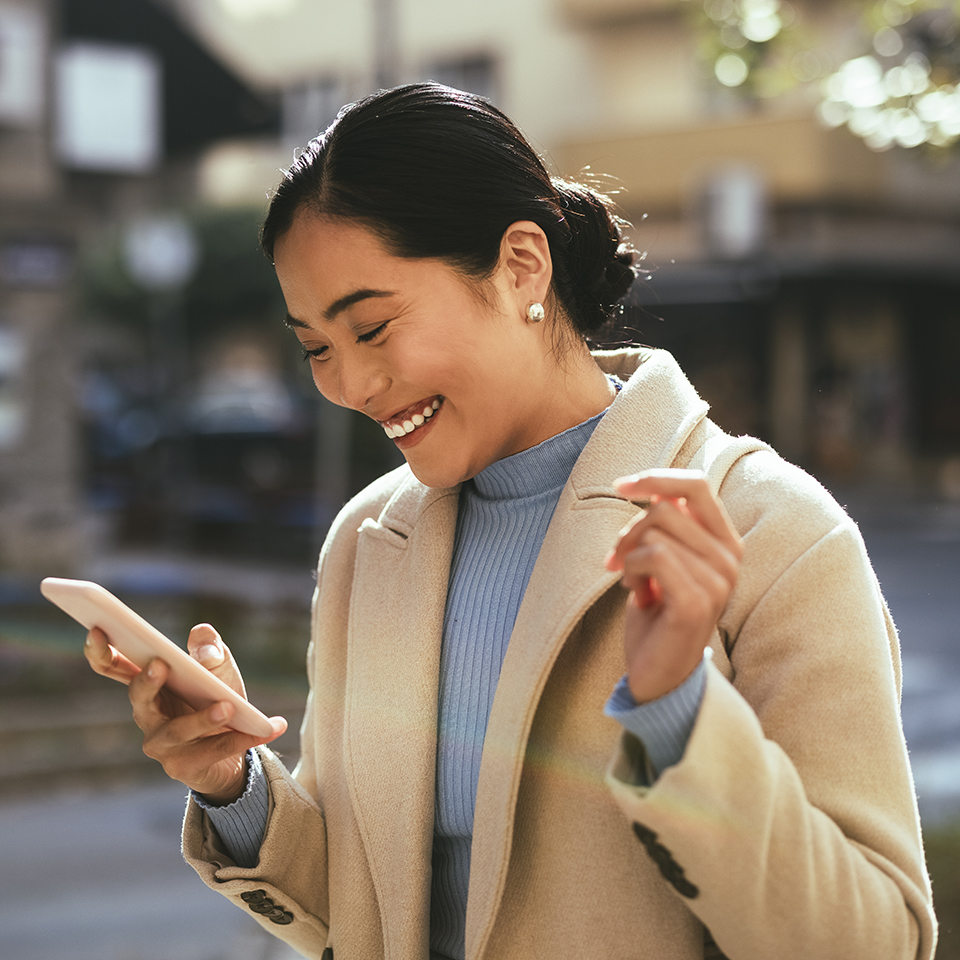 A woman outside looking at a smartphone.