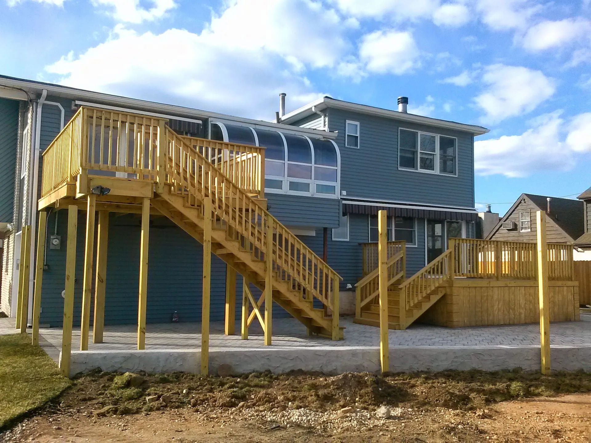 Newly constructed elevated wooden deck with staircase and railings attached to a residential home. The project demonstrates expert carpentry, structural support, accessibility, and attractive outdoor living enhancement.