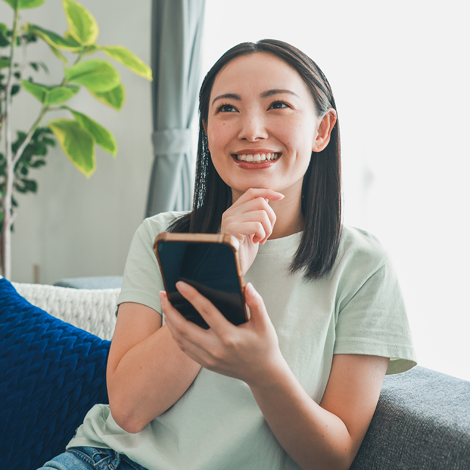 A woman sitting on a couch smiling looking at a phone