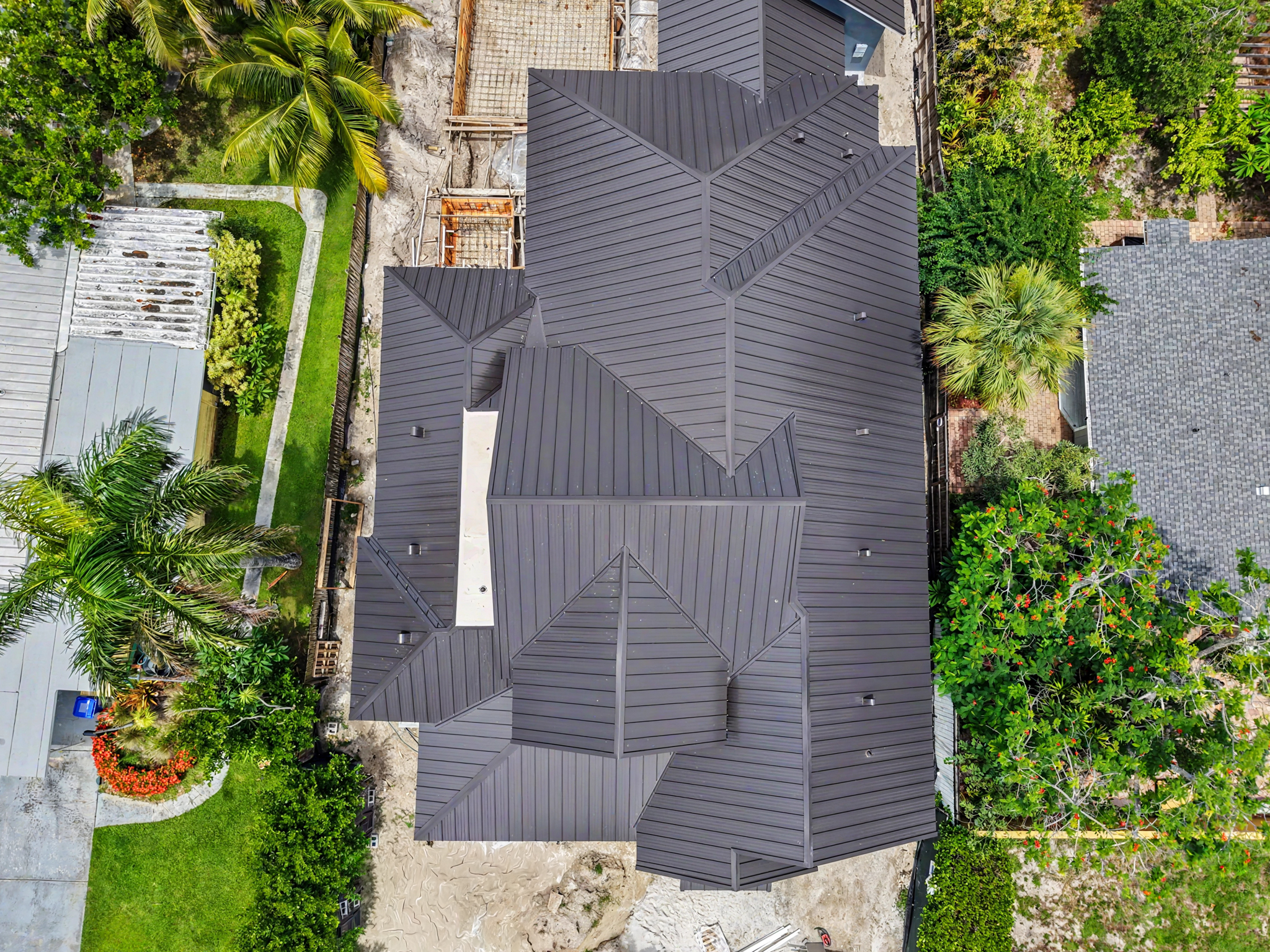 Top-down drone view of a residential dark metal roofing system with multiple intersecting roof secti 